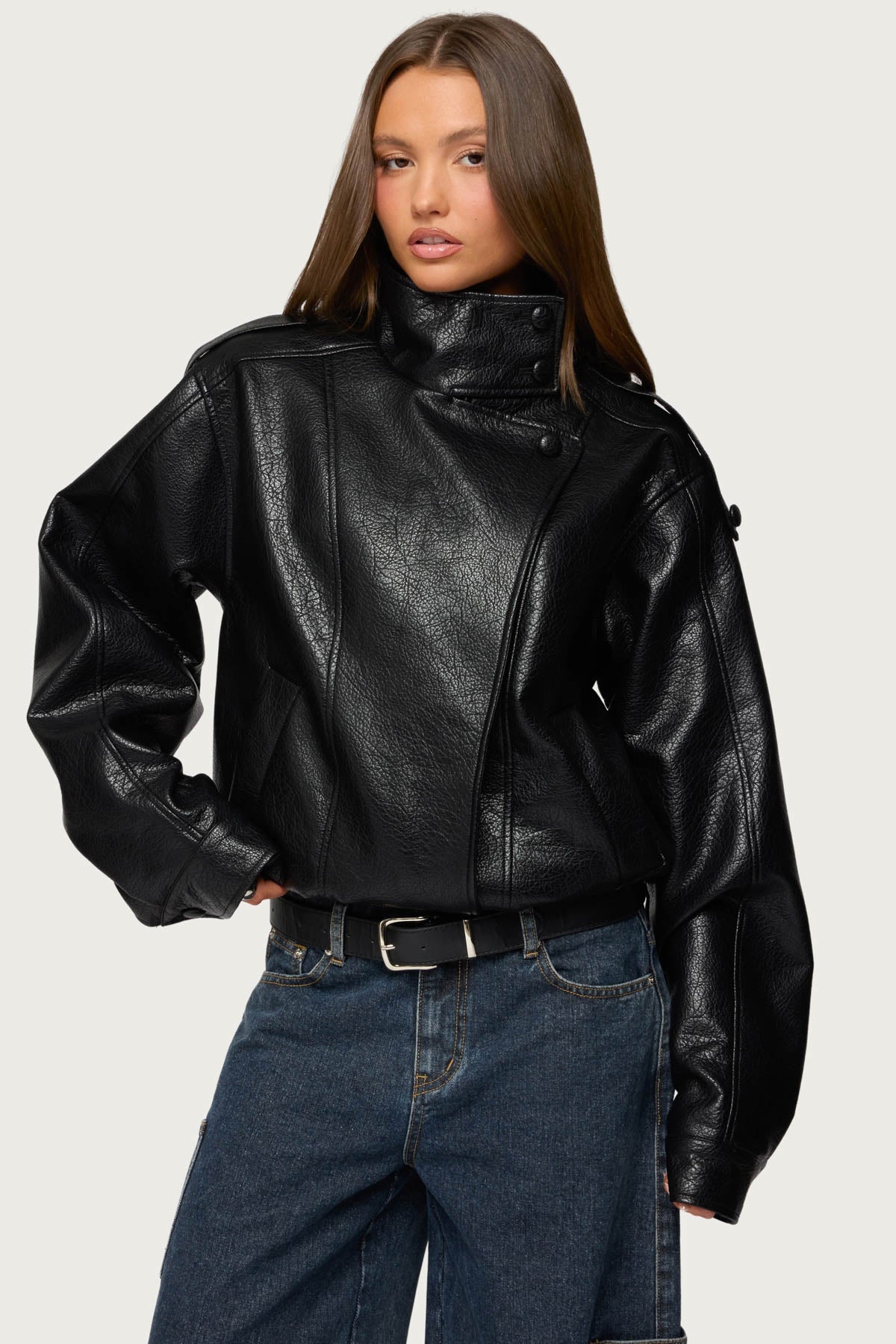 Frau in schwarzer Oversize-Jacke aus Kunstleder mit hohem Stehkragen und asymmetrischer Druckknopfleiste, dazu dunkle Baggy-Jeans