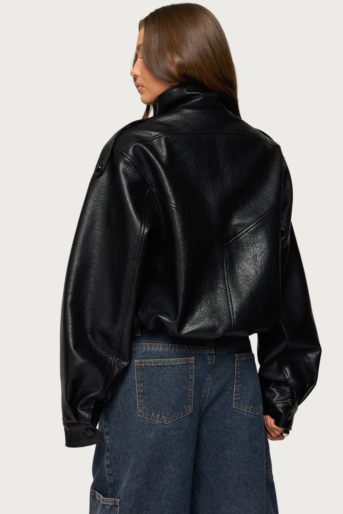 Rückenansicht einer schwarzen Oversize-Kunstlederjacke mit Schulterriegeln, Passennähten, elastischem Saum und Druckknöpfen an den Ärmeln